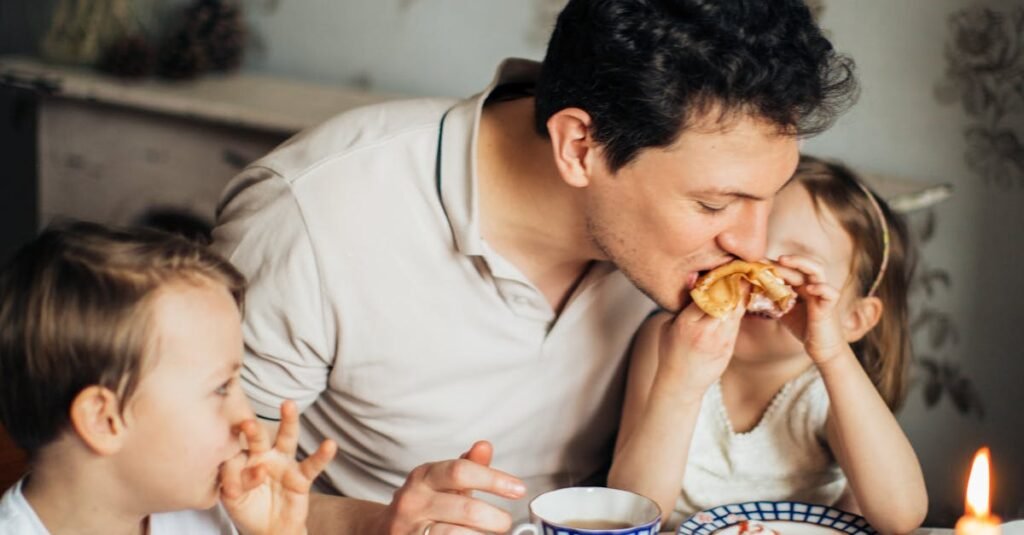 A father and his two children share a joyful meal featuring traditional crepes, creating a warm family moment indoors.